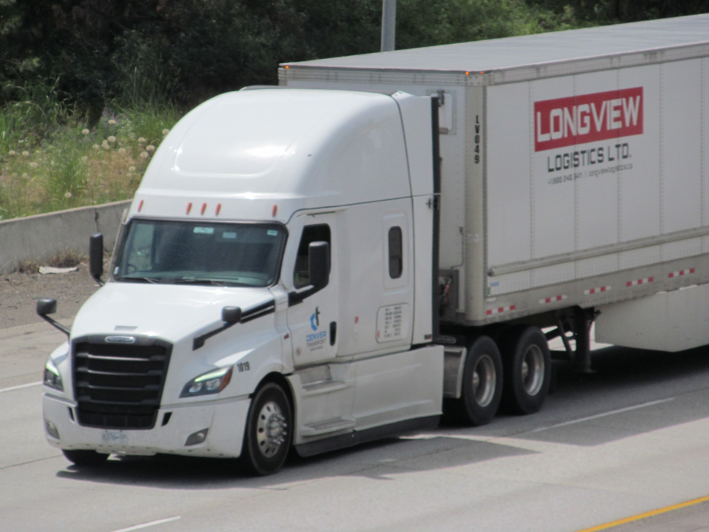 A white Freightliner tractor pulls an enclosed box trailer along Interstate 90 in Spokane, Washington.